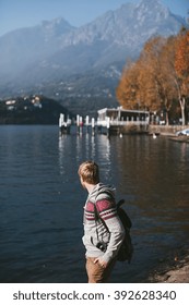 man with a backpack and camera stands on the shore of a mountain lake Como