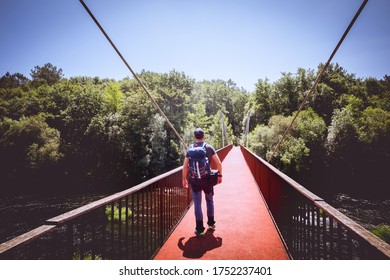 Man with backpack and cap crossing a bridge over a river, in the middle of the forest