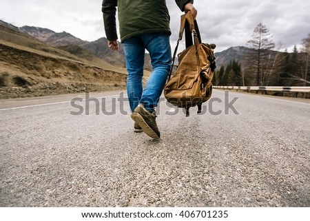 man with backpack in hand walking down a mountain road