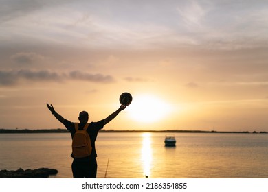 Man with backpack and hat opens his arms by the sea
