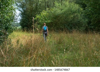 Man with backpack hikes through forest field in summer.