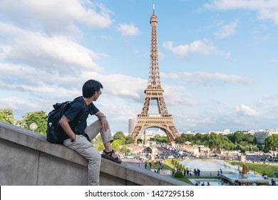 A Man With Backpack Looking At Eiffel Tower, Famous Landmark And Travel Destination In Paris, France. Traveling In Europe In Summer