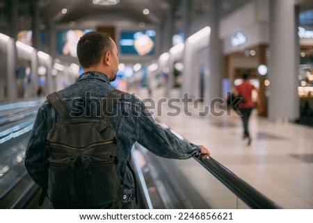A man with a backpack moves to the gate on a travelator at the airport. A young tourist guy with hand luggage in a modern large airport terminal