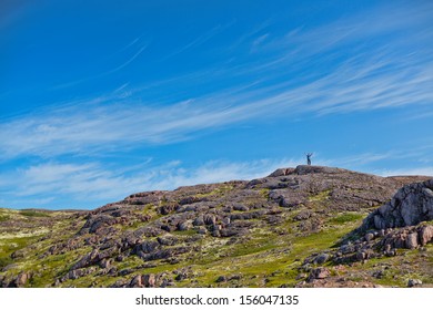 Man with a backpack on a mountain spread wide his hands in the summer against a blue sky with clouds