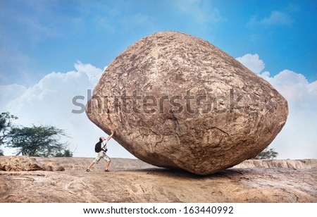 Man with backpack pushing a huge stone in Mamallapuram cave complex, Tamil Nadu, India