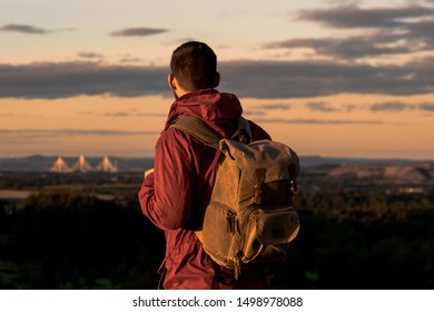 Man with a backpack and a red jacket looking at sunset over a city on the distance