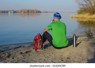 Man with backpack is resting on the riverside. Autumn.