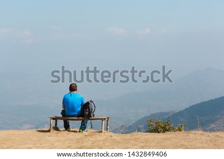 A man with a backpack sits on a bench looking to the horizon. Kathmandu. Nagarkot. View point on the mountains of Nepal. Landmark.
