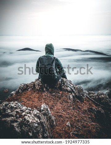 Man with Backpack sitting alone on Mountain Peak over a sea of clouds in austria
