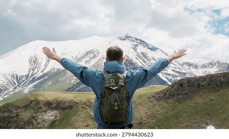 Man with backpack standing before snow covered mountain range, arms outstretched embracing wilderness landscape, adventure travel concept, hiking expedition, freedom, exploration, outdoor achievement