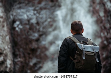 Man with backpack standing in front of waterfall