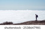 A man with a backpack standing looking at the cloud-filled horizon. 