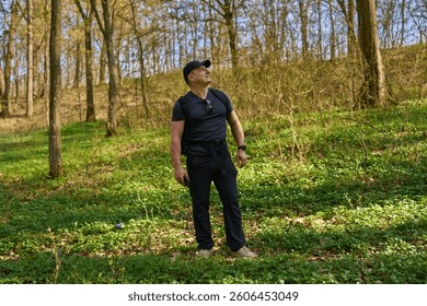 Man with backpack standing in spring forest looking up into trees
