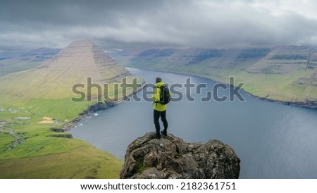 Man with backpack, traveler or explorer standing on top of mountain or cliff and looking down valley. Concept of discovery, exploration, tourism. Villingardalsfjall and Cape Enniberg Faroe Islands