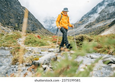 Man with backpack and trekking poles crossing mountain creek during Makalu Barun National Park trek in Nepal. Mountain hiking and active people concept image.