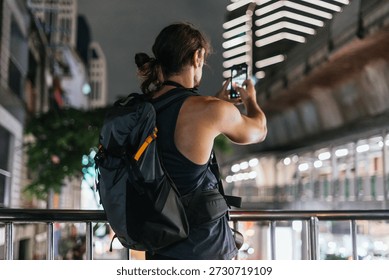 Man with backpack using smartphone to capture urban scene at night