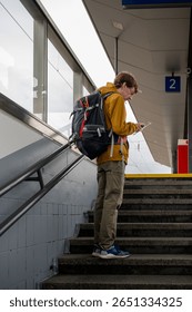 Man with backpack using smartphone at train station stairs