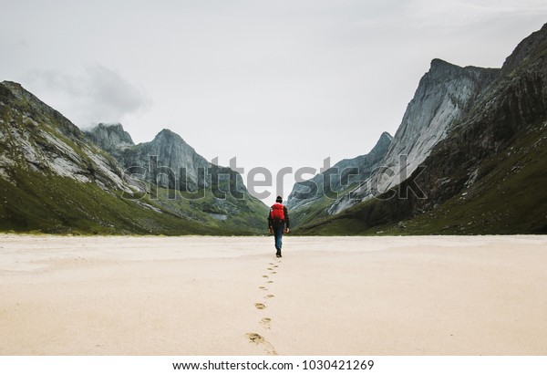Man with backpack walking away alone at sandy\
beach in mountains Travel lifestyle concept adventure outdoor\
summer vacations in Norway wild nature\
