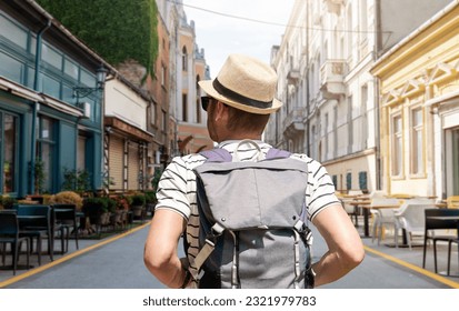 Man with backpack walking down street in European city.