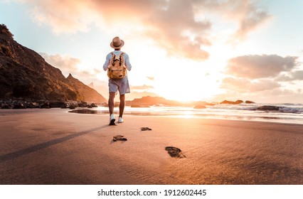 Man with backpack walking on the beach at sunset - Travel lifestyle concept - Golden filter - Powered by Shutterstock