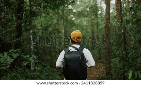 A man backpacker traveling alone in forest wild. Young man hiking trip through the green forest with backpacks. Asian man traveler explore while walking in green forest. Travel and backpack concept