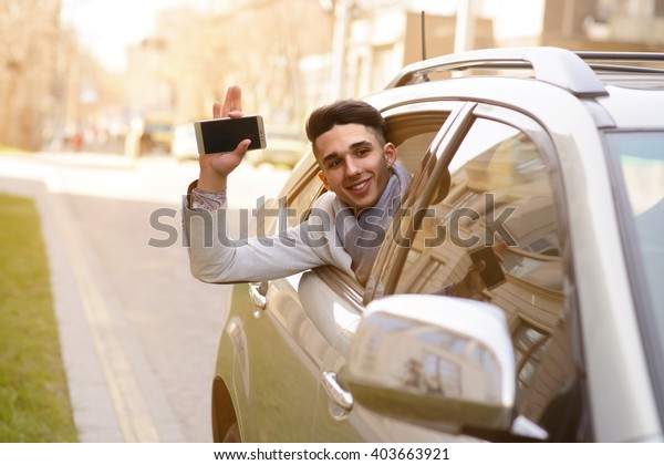 the man in the\
backseat of a luxury car waving his hand holding a cell phone and\
looks out the car window
