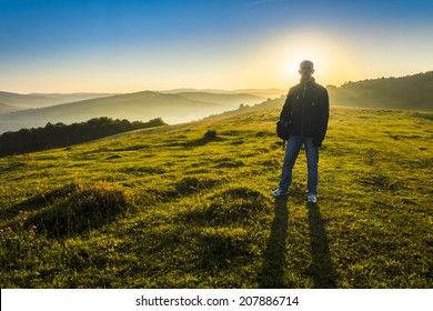 Man With Bag In Mountains Backlit By Sun Early In The Morning