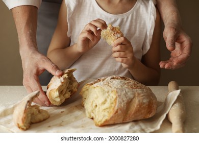 A Man Baker Father In An Apron Breaks Freshly Baked Wheat Bread With His Hands With A Little Girl Daughter. Selective Focus. Concept: Baking Bread At Home With Children.