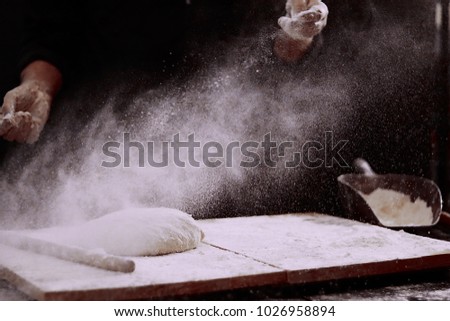 Man baking bread. Sprinkling some flour on dough. Hands kneading dough.