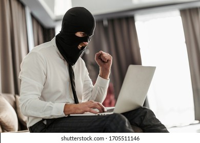 A Man In A Balaclava Mask And A White Office Shirt, Sitting At A Laptop And Trying To Anonymously Go Live For A Stream