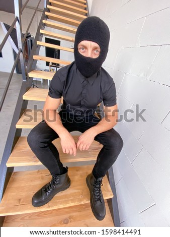 A man in a balaclava is sitting on the stairs.