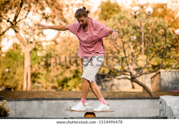 Man balancing on the\
balance board on the concrete steps in the park in the background\
of yellow trees