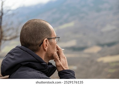 A man with a bald head and glasses is smoking a cigarette. Concept of solitude and contemplation, as the man is alone in a vast, open field - Powered by Shutterstock