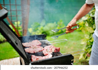 Man at a barbecue grill preparing meat for a garden party