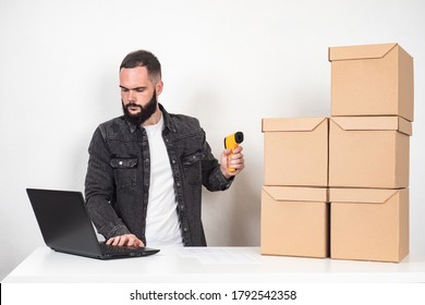 A man with a barcode reader and a laptop. Storekeeper next to cardboard boxes. Inventory. Product packaging marking. Encoding of product information. - Shutterstock ID 1792542358