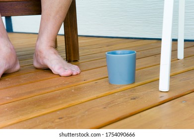 A man with bare feet sitting next to tea mug placed on the wooden floor - Powered by Shutterstock