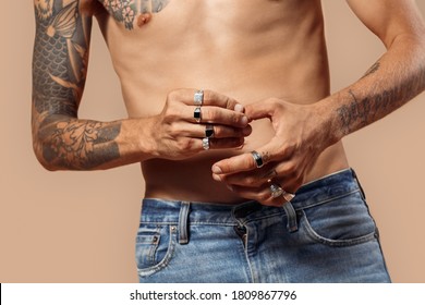 Man with bare upper body studio standing isolated on beige background touching fingers wearing rings