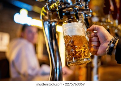 man bartender hand at beer tap pouring a draught beer in glass serving in a restaurant or pub - Powered by Shutterstock