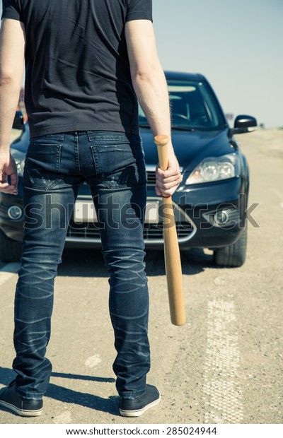 Man with\
baseball bat on the road before the\
car