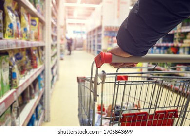 Man with a basket walks in a supermarket. Hand and part of the basket in focus, blurred background - Shutterstock ID 1705843699