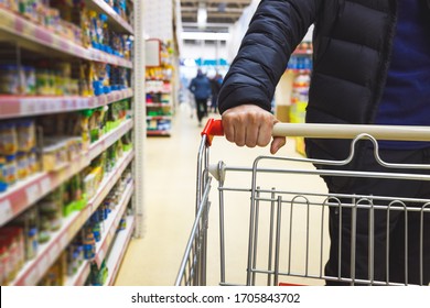 Man with a basket walks in a supermarket. Hand and part of the basket in focus, blurred background - Shutterstock ID 1705843702