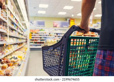 Man with a basket walks in a supermarket. Hand and part of the basket in focus, blurred background - Shutterstock ID 2199674655