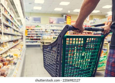 Man with a basket walks in a supermarket. Hand and part of the basket in focus, blurred background - Shutterstock ID 2206982127