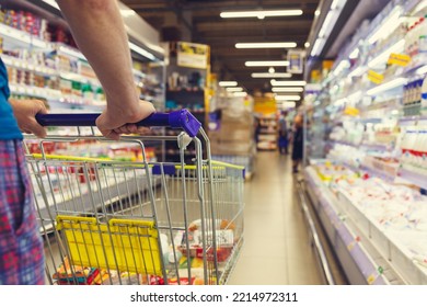 Man with a basket walks in a supermarket. Hand and part of the basket in focus, blurred background - Shutterstock ID 2214972311