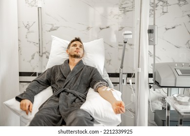 Man In Bathrobe Lying On Medical Couch During Blood Wash Procedure With Catheter In His Arm At Medical Centre