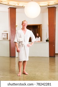 A man in a bathrobe standing in a reception of a spa, looking at the camera