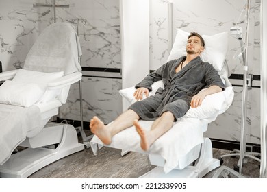 Man In A Bathrobe Is Waiting For A Blood Washing And Vitaminization Procedure Or Taking Blood For Tests In A Medical Center. Lying Relaxed On Comfortable Medical Couch