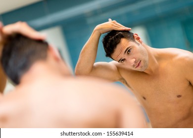 Man In The Bathroom Looking In A Mirror And Fixing His Hair 