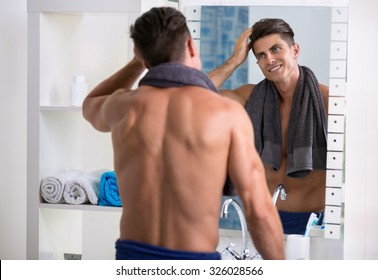 Man In The Bathroom Looking In A Mirror And Fixing His Hair.