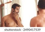 Man, bathroom and skincare or cosmetics in mirror for morning routine, grooming and self care for beard. Person, topless and cleaning face for glowing skin, hygiene and getting ready with reflection